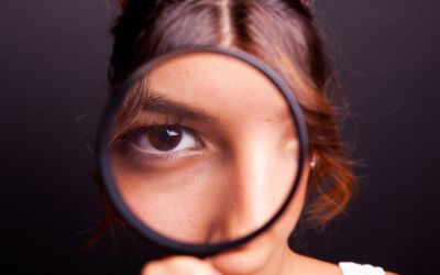 Photo of a girl looking through a magnifying glass at the camera, to illustrate the article Why We Need Spiritual Discernment Now More Than Ever